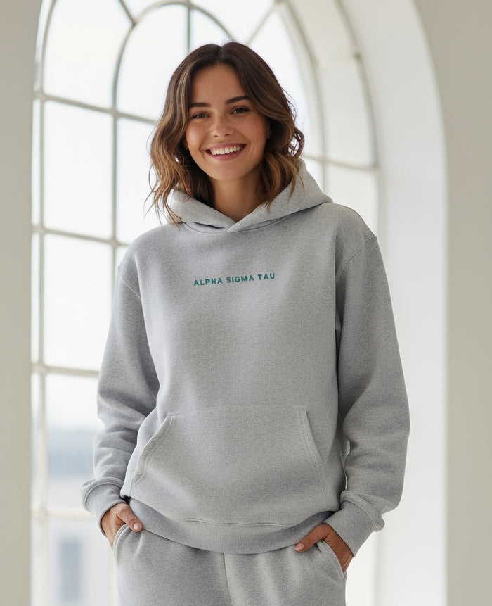 Woman indoors smiling in a gray Alpha Sigma Tau hoodie with matching sweatpants