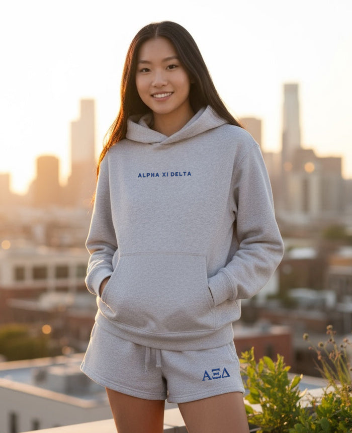 Woman in gray Alpha Xi Delta hoodie and matching shorts on a city rooftop