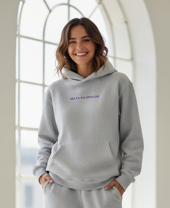 Person wearing gray Delta Phi Epsilon hoodie indoors, smiling