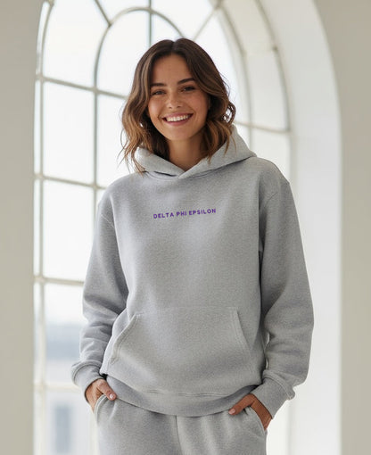 Person wearing gray Delta Phi Epsilon hoodie indoors, smiling