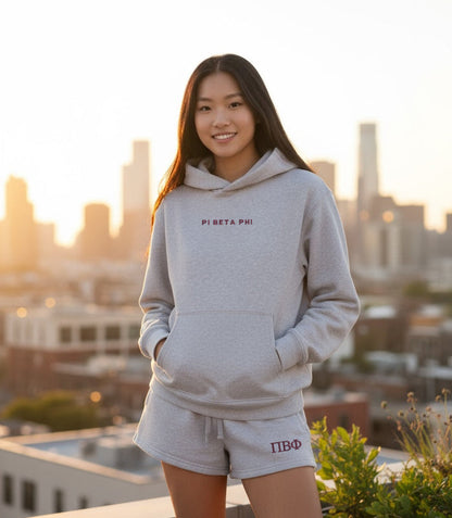Individual wearing gray hoodie and shorts with Pi Beta Phi embroidery, cityscape background